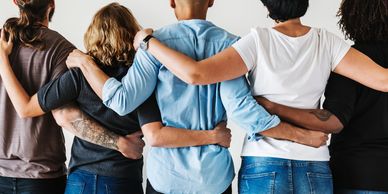 Group of diverse people standing back to back with arms around each other.
