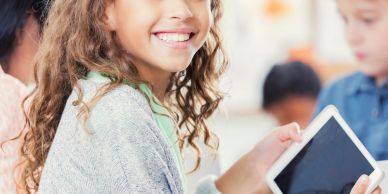Smiling girl holding a tablet in a classroom setting.