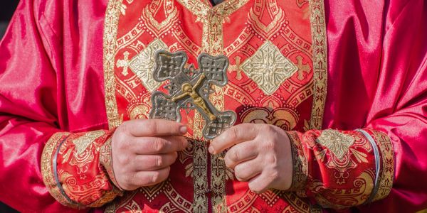 Person holding a metal cross in ornate red and gold robe.