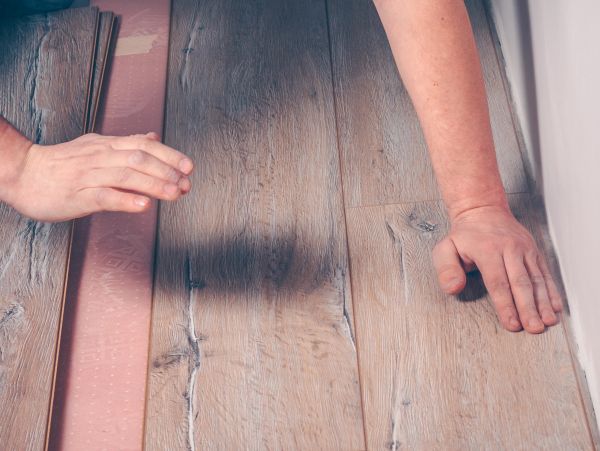 Hands installing wood laminate flooring with underlayment.