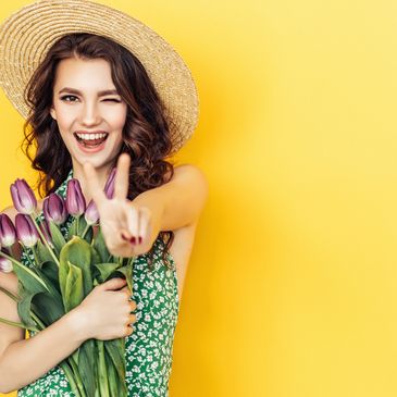 Femme souriante avec chapeau tenant un bouquet de tulipes.