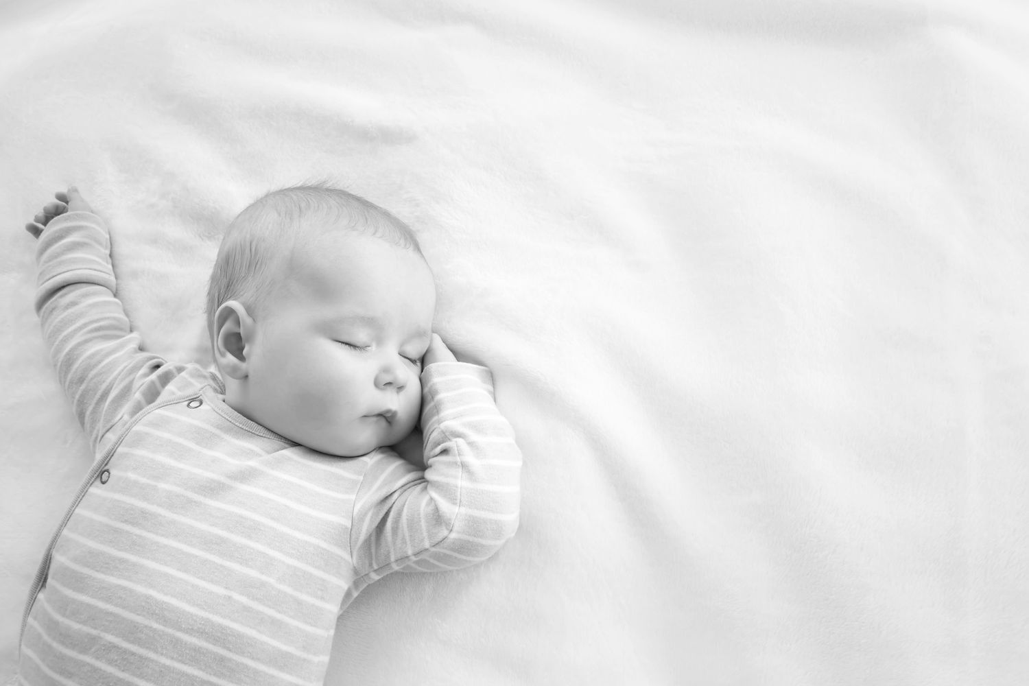 Sleeping baby in a blue striped onesie lying on a soft white surface.