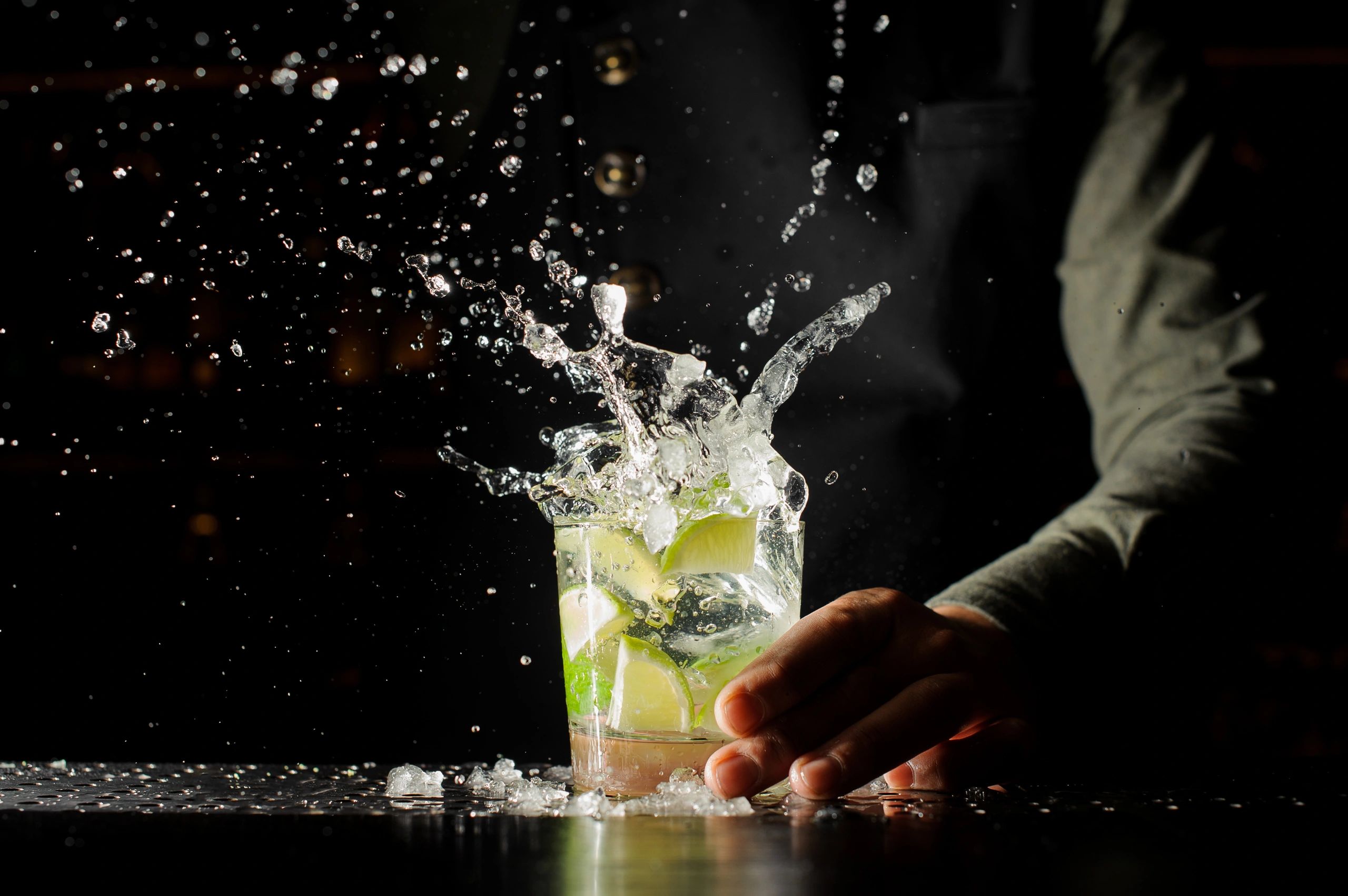 Splash of a lime-infused cocktail held by a hand in low light.