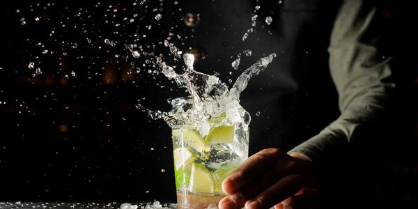 Hand holding a cocktail glass with lime and ice splashing out.