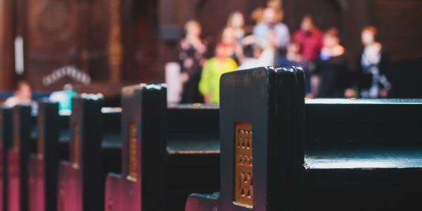 Close-up of empty church pews with blurred people in background.