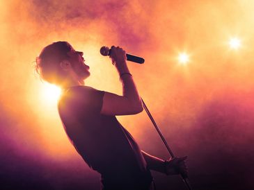 A singer passionately performing on stage with vibrant orange lighting.