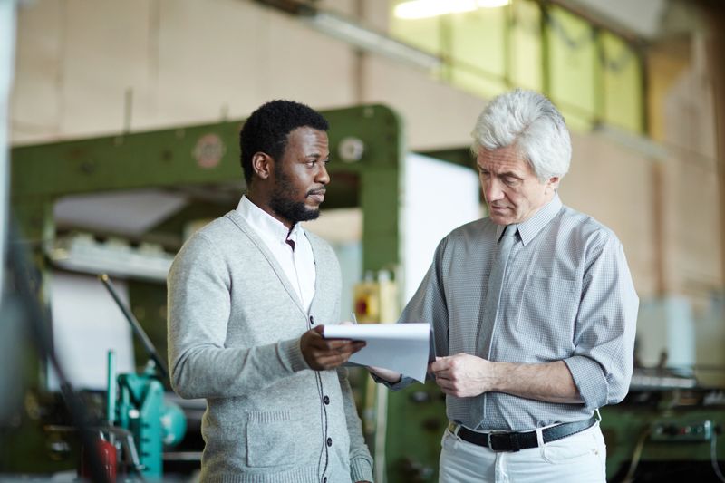 Serious confident African-American manager giving papers for signing to boss while they planning new strategy of printing plant development