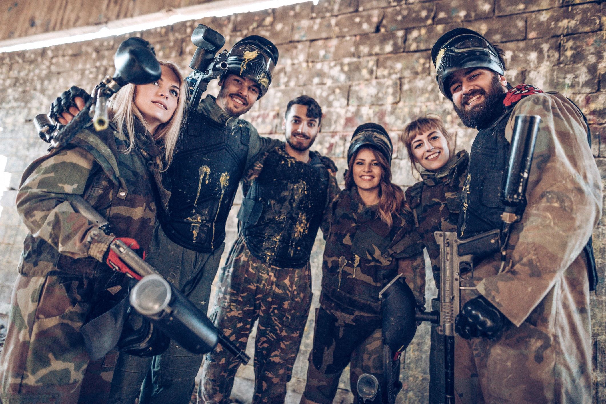 Group of friends in paintball gear smiling and posing for a photo.