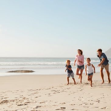 Family of four happily running on a sunny beach with mountains in the background.