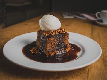 Chocolate cake with ice cream and crunchy topping on a white plate.