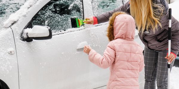 Woman and child clearing snow from a white car in winter.