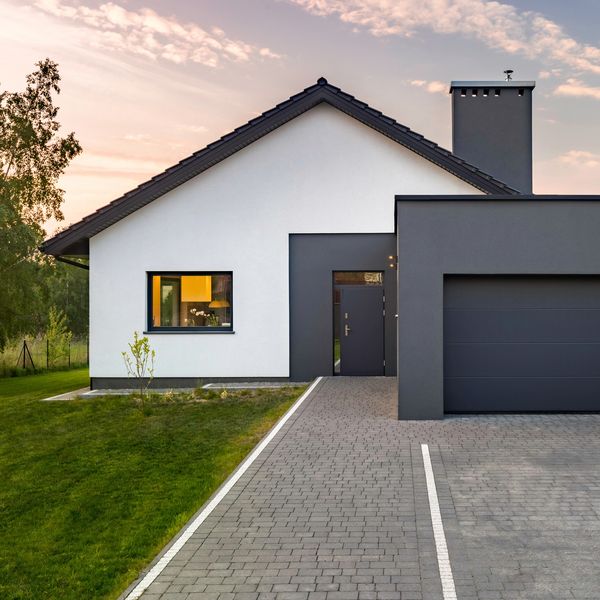 Modern house with white and gray walls, a paved driveway, and a green lawn at sunset.