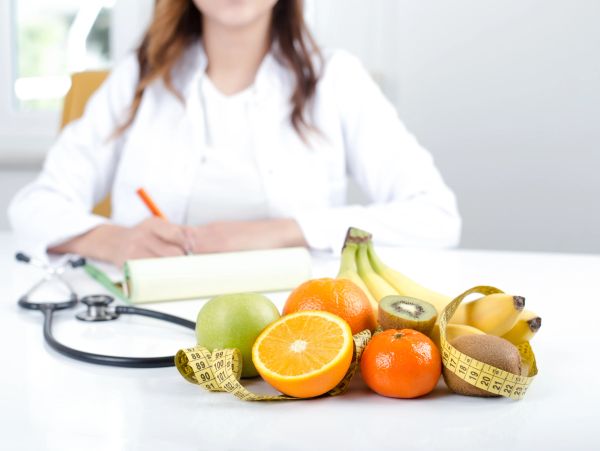 A nutritionist with fresh fruits and a measuring tape on a table.