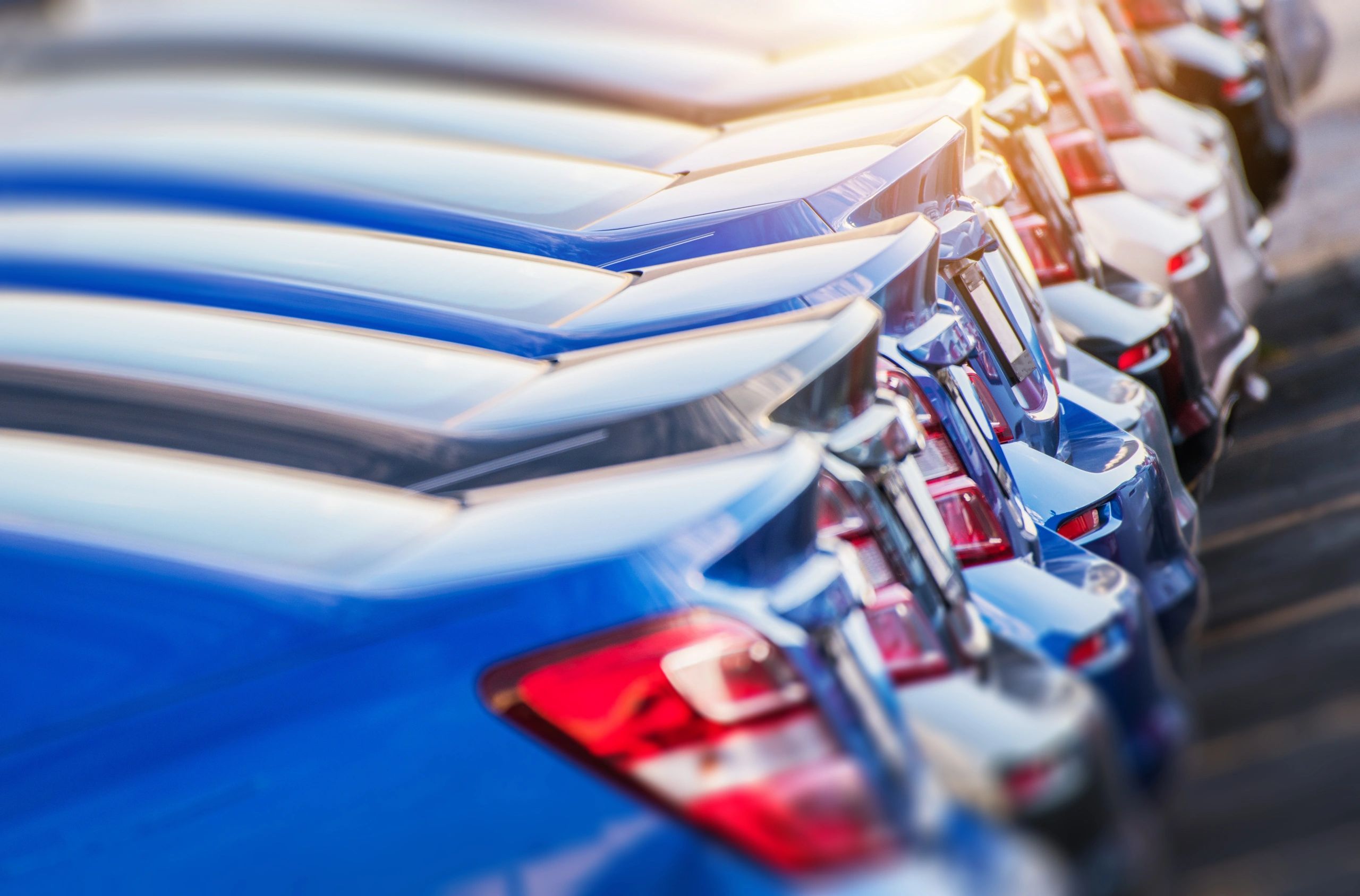 Row of shiny new cars parked closely together in sunlight.