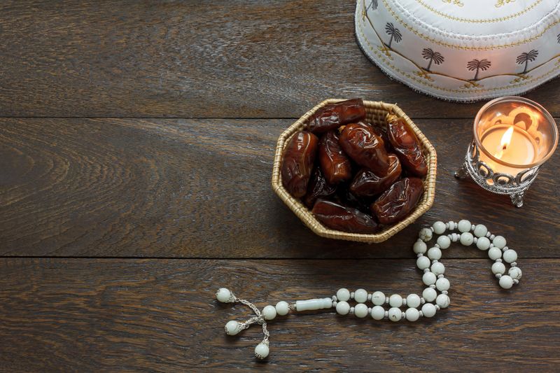 Table top view aerial image of decoration Ramadan Kareem holiday background.Flat lay date in wood basket with white prayer beads & lighting.The blackboard space on modern rustic brown wood at office desk.