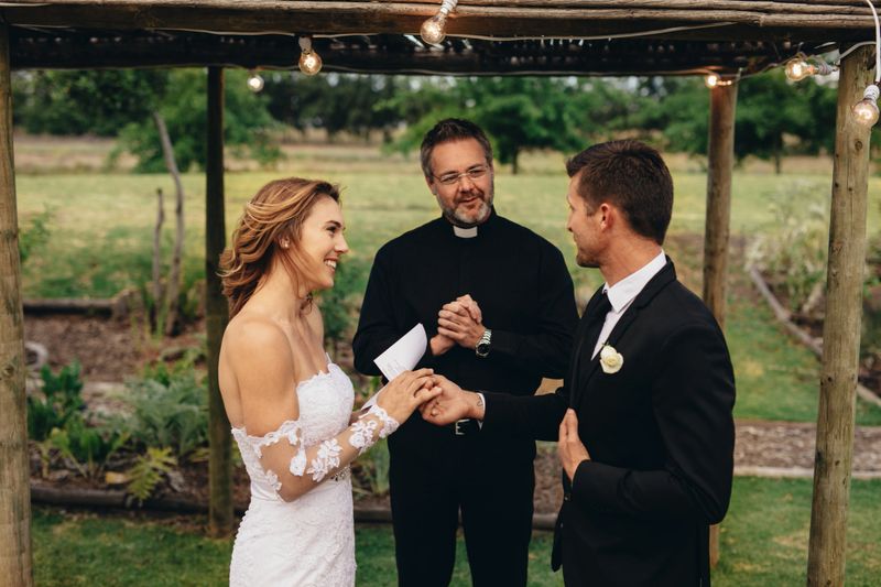 Happy young bride and groom exchanging wedding vows on wedding ceremony in front of priest. Couple reading wedding vows for each other.