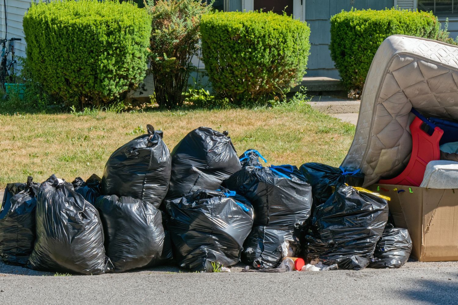 A pile of black garbage bags and discarded furniture outside a house.