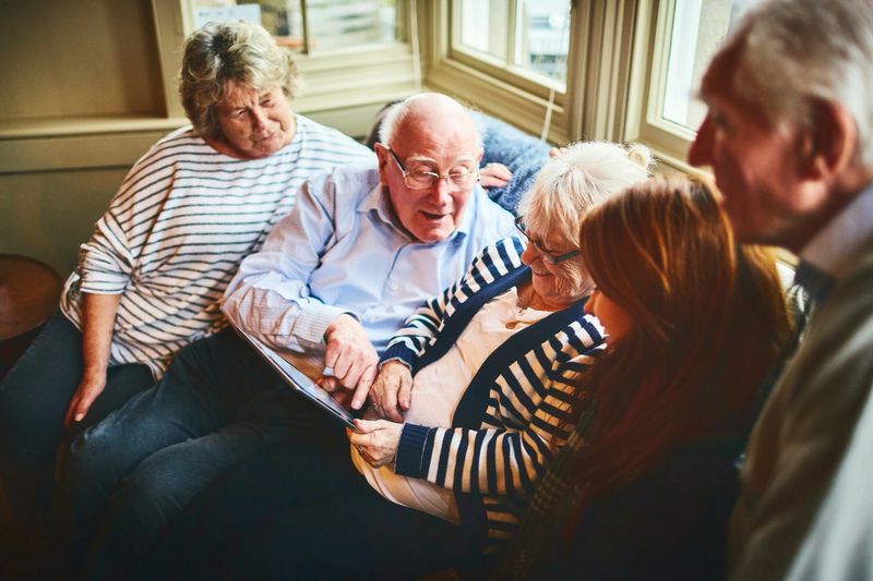 Group of elderly people with young woman sitting on a sofa and using digital tablet