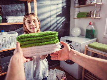 A girl hands over folded towels in a laundry room.