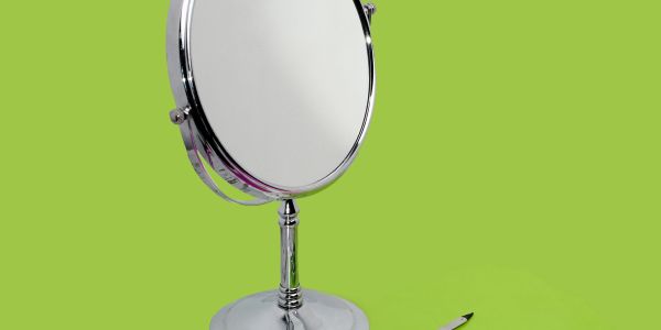 A round tabletop mirror with a pen lying beside it on a green background.