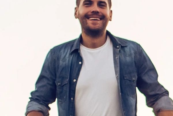 A smiling man wearing a denim shirt over a white t-shirt.