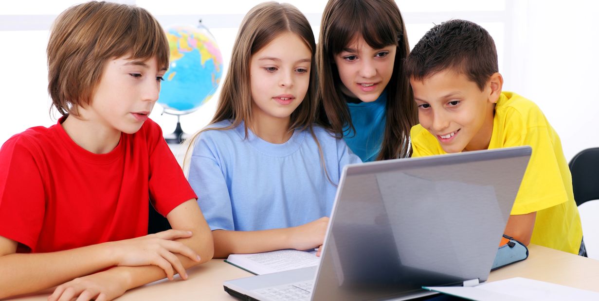 Four children gathered around a laptop, focused and engaged.