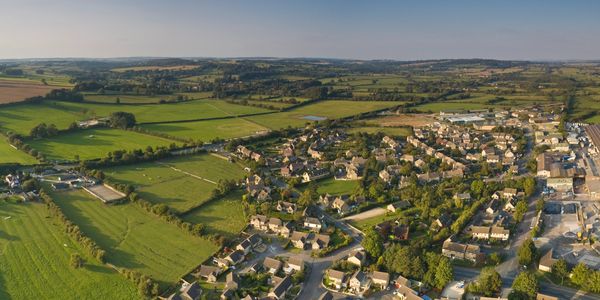 Aerial view of a countryside town with fields and houses under a clear sky.
