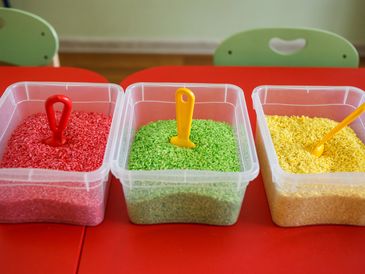 3 clear tupperware boxes filled with red, green and yellow rice and a tool to explore in each box.