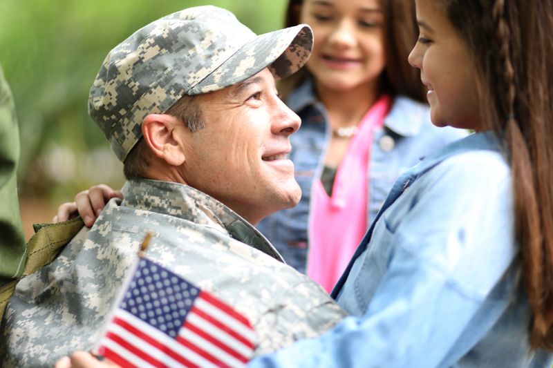 Family welcomes home a USA army soldier.  The children excitedly hug father holding American flags.