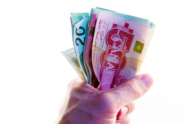 Hand holding Canadian dollar bills of various denominations.