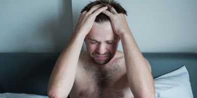 Man in bed holding his head, appearing distressed or in pain.