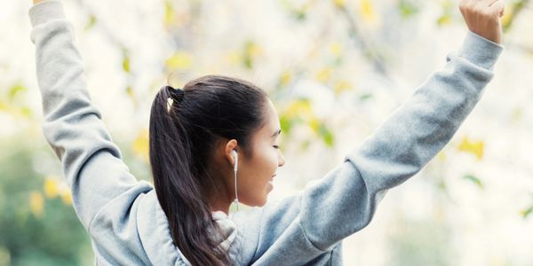 A woman in a gray hoodie stretches outdoors with earbuds in.
