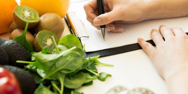 Person writing on a clipboard next to fresh fruits and vegetables.