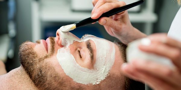 A man getting a white facial mask applied with a brush.