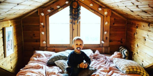 Child sitting on a bed in a wooden attic room.