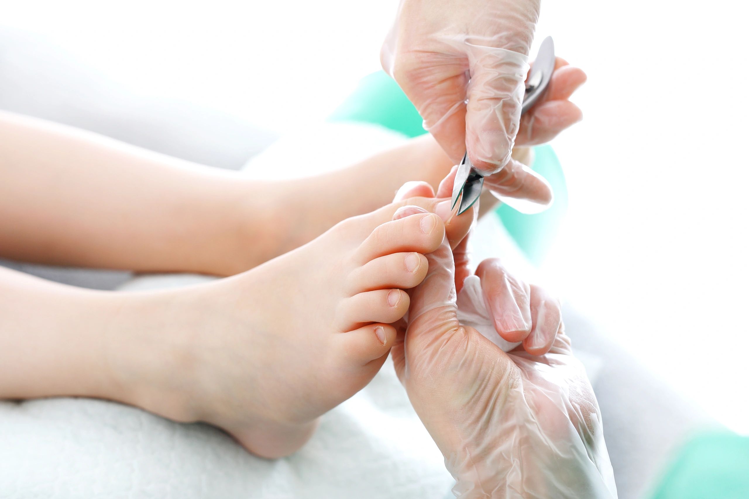 Gloved clinician trimming a patient’s toenails with nail clippers.