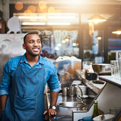 Smiling barista in apron standing behind the counter at a coffee shop.