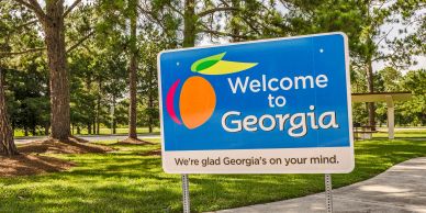 Welcome sign for Georgia with peach logo in a park setting.