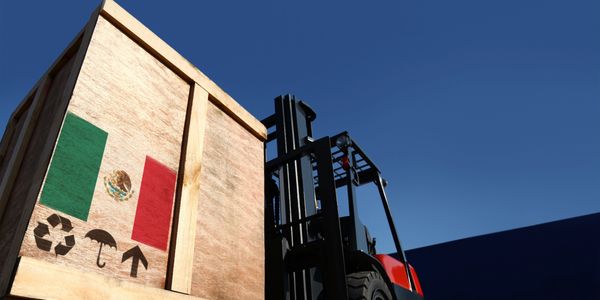 A forklift lifting a wooden crate with the Mexican flag and handling symbols.
