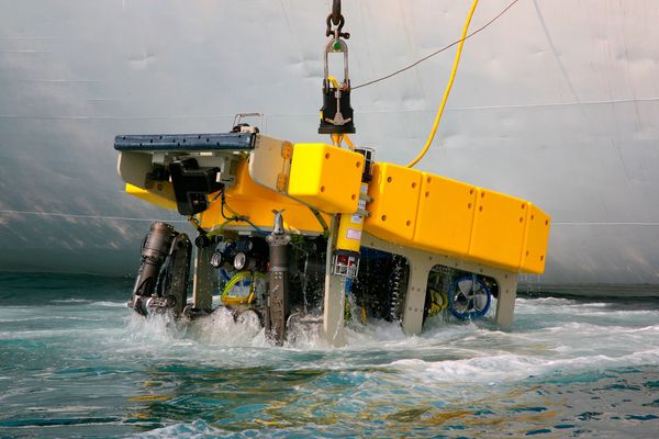 A yellow underwater remotely operated vehicle (ROV) being lowered into the water.