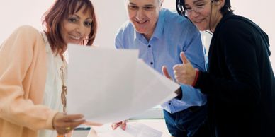 Three colleagues smiling and reviewing documents together in a bright office.