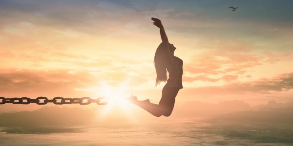 Silhouette of a woman breaking free from chains at sunrise, symbolizing freedom.
