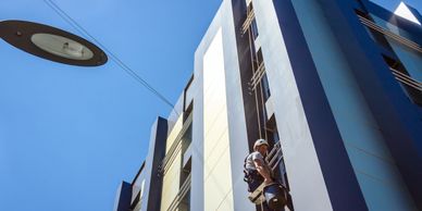 Person rappelling down a tall building under a clear blue sky.