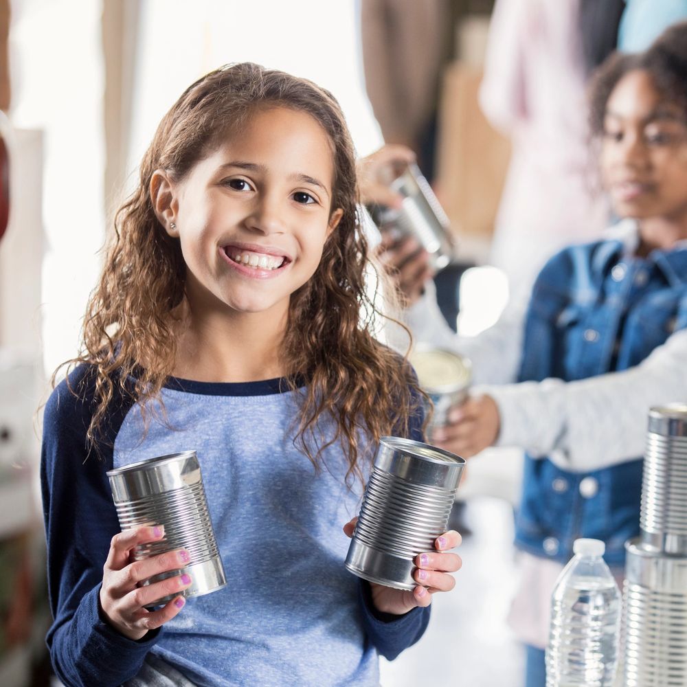 Smiling girl holding canned food while volunteering.