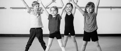 Four children posing with arms raised in a dance studio.