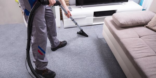 A person vacuuming a gray carpet in a modern living room.