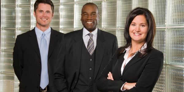 Three professionals in business attire smiling confidently indoors.