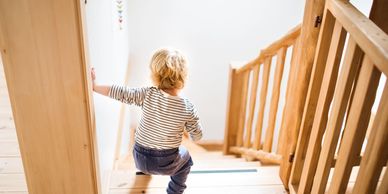 Toddler cautiously descending wooden stairs inside a home.