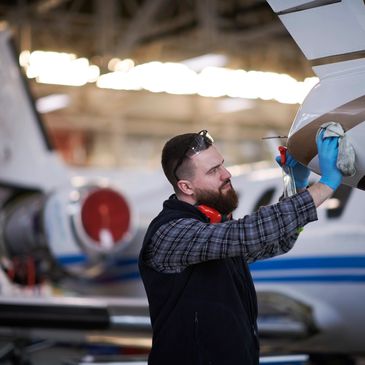 A technician cleaning the exterior of a private jet in a hangar.