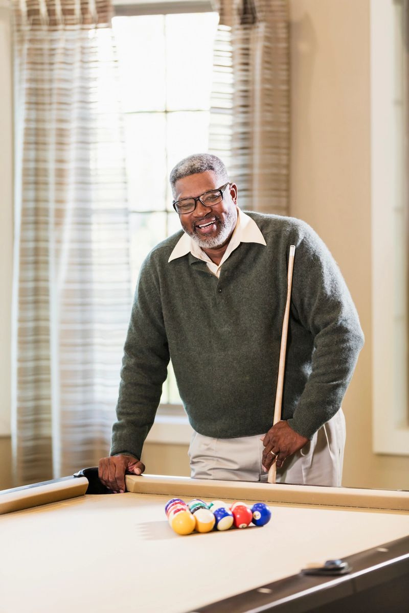 A senior African-American man in his 60s playing billiards. He is standing at one end of the pool table, holding a cue stick, ready to start the game.